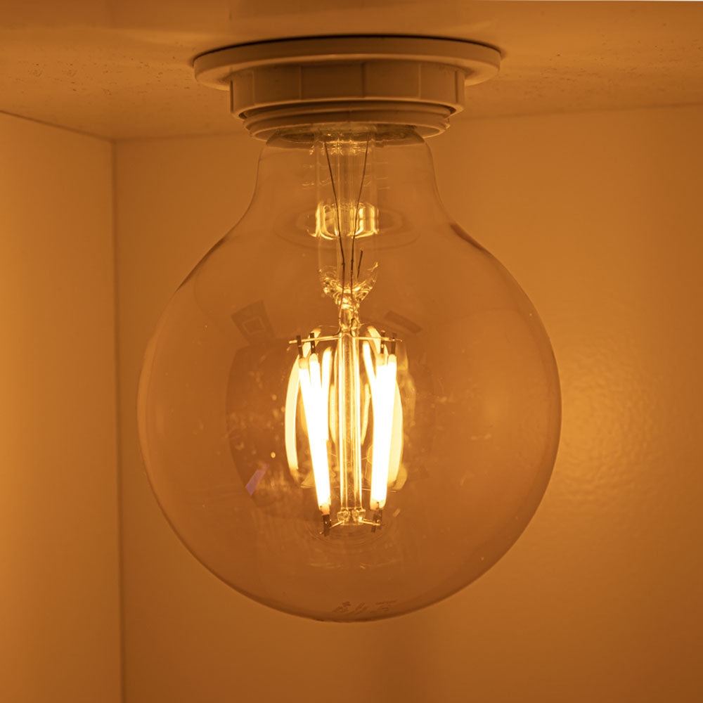 Nahaufnahme einer brennenden LED-Glühbirne mit warmweißem Licht, an der Decke montiert, von unten betrachtet.
