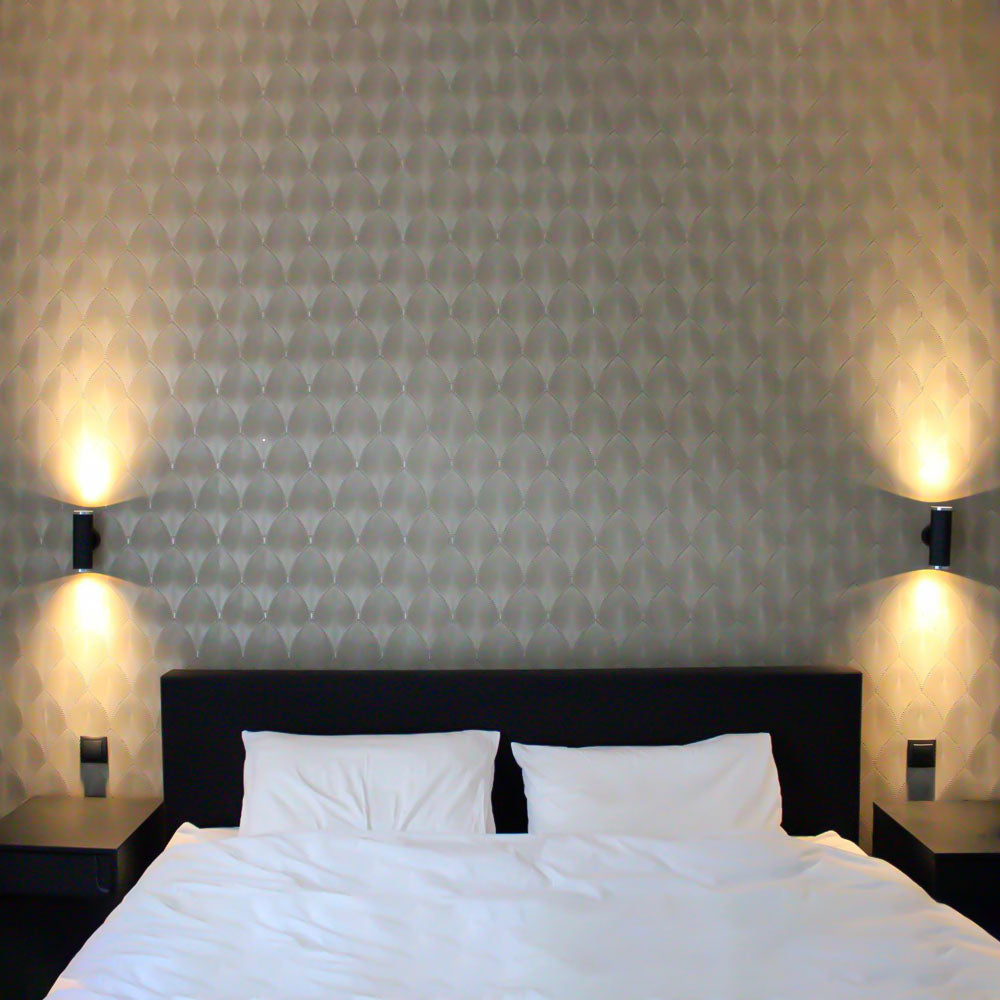 Ein modernes Doppelbett mit weißer Bettwäsche, einem schwarzen Kopfteil und Nachttischen, fotografiert vor einer hellgrauen Wand mit einem eleganten Muster und stimmungsvoller Beleuchtung auf beiden Seiten.
