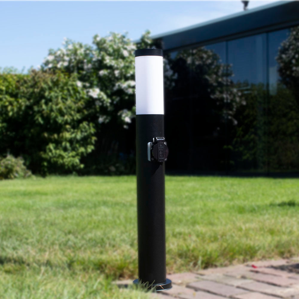Schwarze Gartenlampe mit Fassung in zylindrischer Bauform, Frontansicht, platziert auf einer Rasenfläche neben einem modernen Haus mit Glasfassade.