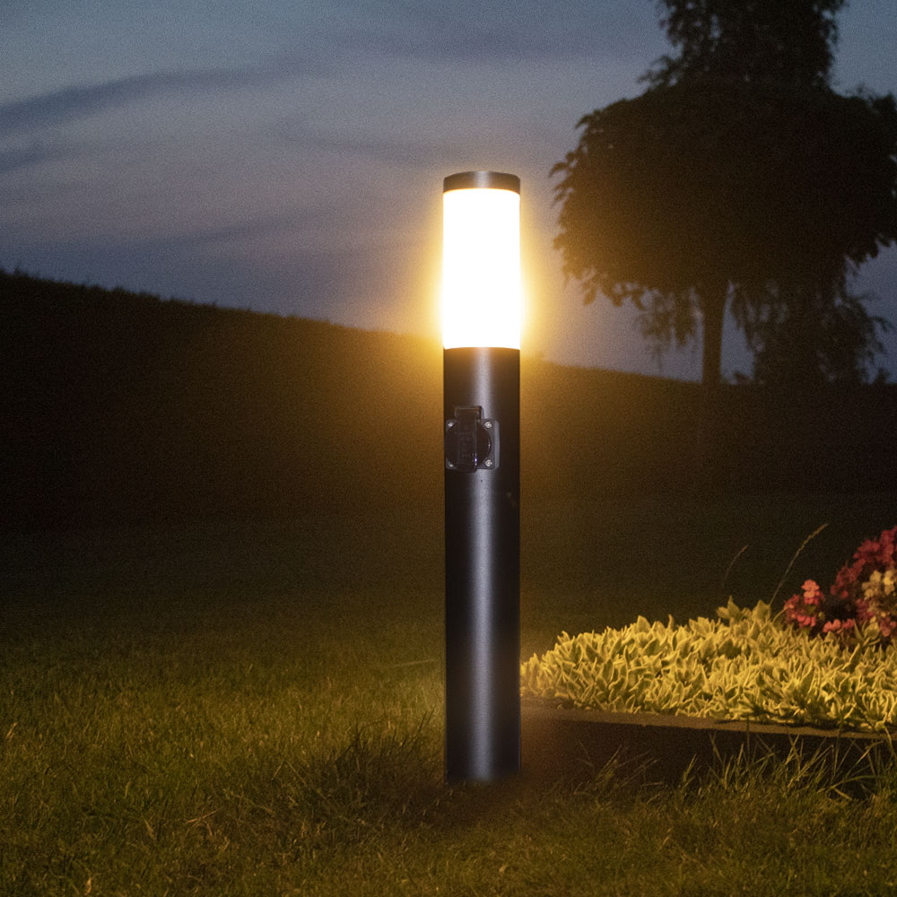 Stehende Außenleuchte mit Steckdose, schwarz, stimmungsvolle Beleuchtung im Garten bei Dämmerung - Frontansicht.