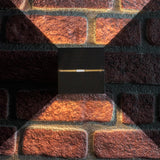 Schwarze, moderne Up- und Down-Wandlampe an einer roten Backsteinwand, Vorderansicht, mit dekorativer Up- und Down-Beleuchtung.