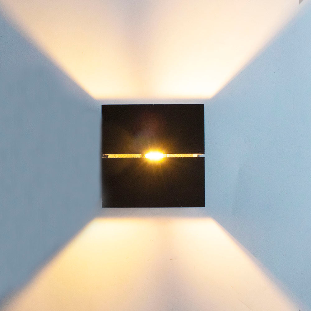 Schwarze, moderne Wandleuchte mit Auf- und Ablicht, Frontansicht mit warmer LED-Beleuchtung, die ein stimmungsvolles Lichtmuster an der Wand erzeugt.