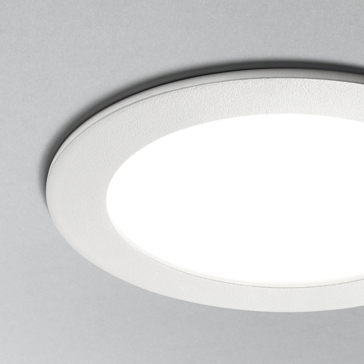 Nahaufnahme eines runden, weißen LED-Deckeneinbaustrahlers vor grauem Hintergrund, mit minimalistischem und modernem Design.