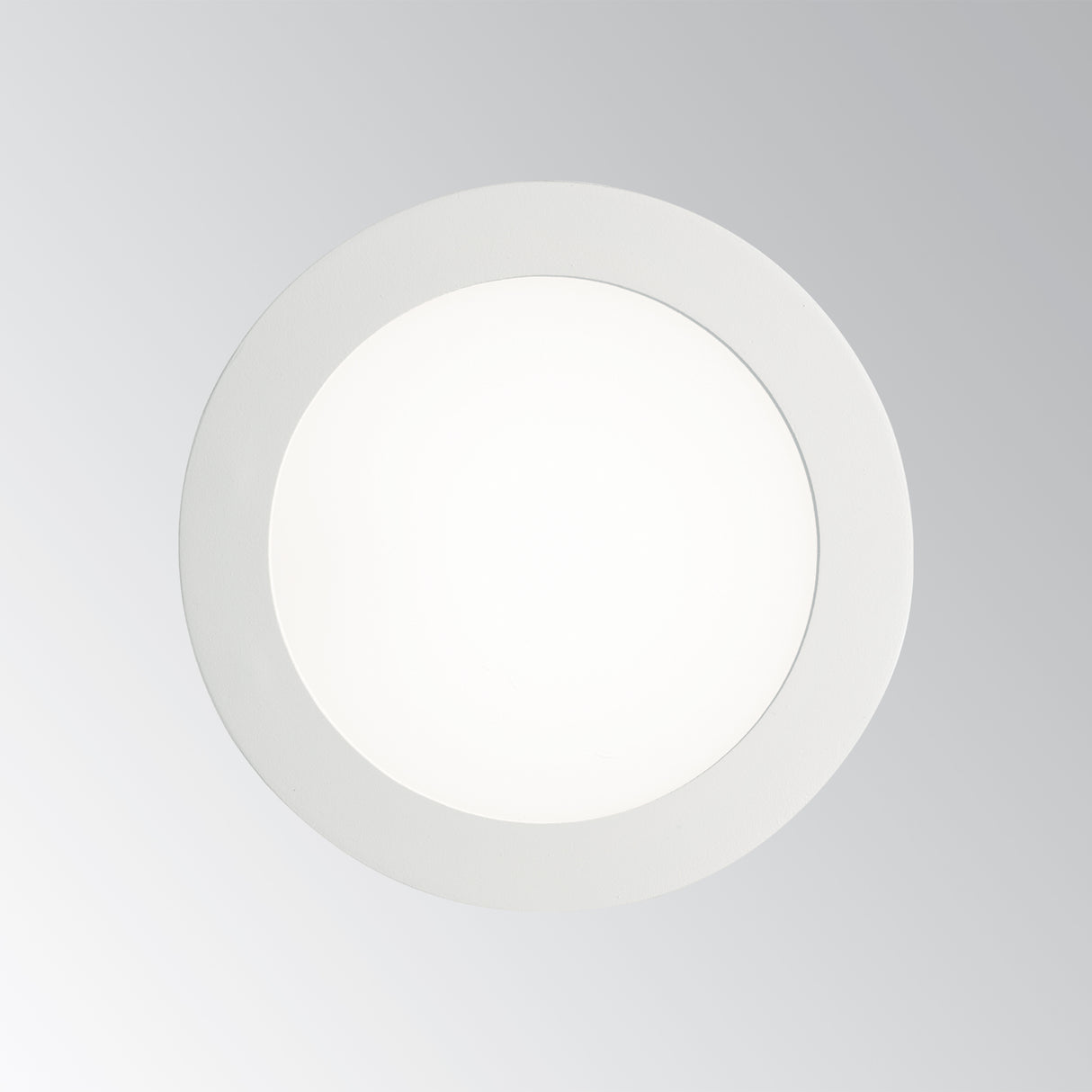 Runder weißer LED-Einbaustrahler in flacher Bauform, von vorne fotografiert vor grauem Hintergrund.