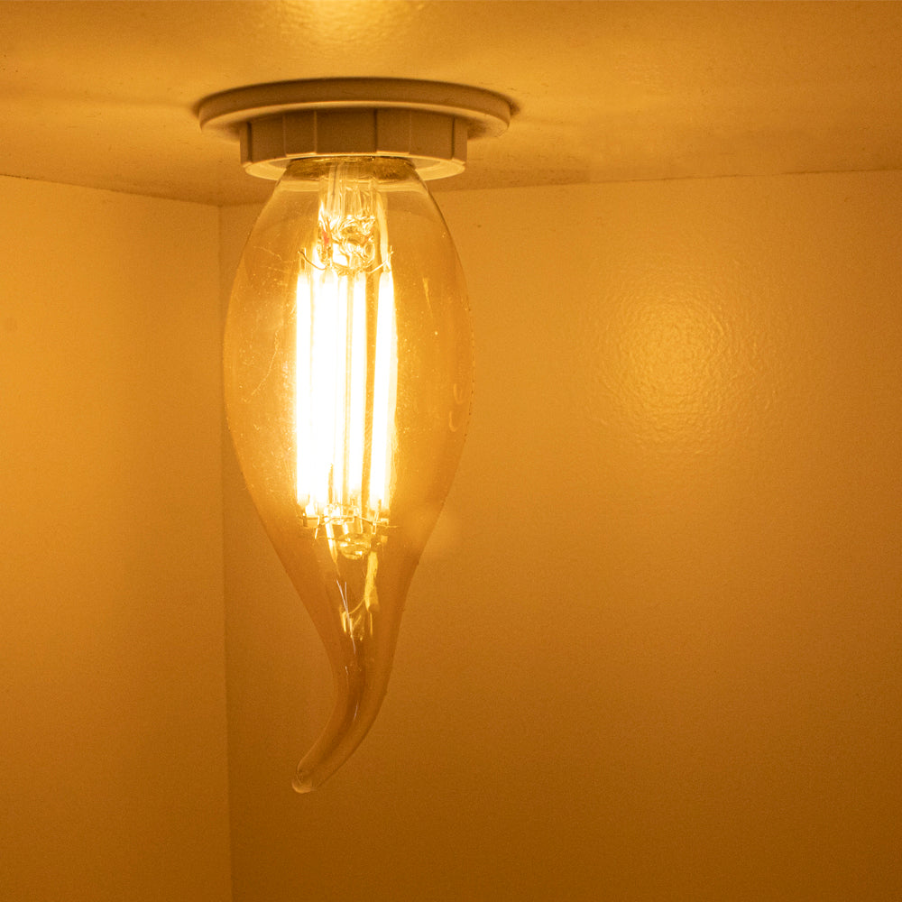 Dekorative Deckenleuchte mit einer warmweißen LED-Flammen-Filamentlampe in Tropfenform, von unten betrachtet in einem warm beleuchteten Raum.
