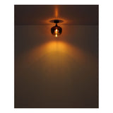 Nahaufnahme einer brennenden Kupferdeckenlampe von vorne, die vor einer dunklen Wand und Decke für warmes, stimmungsvolles Licht sorgt.