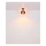 Nahaufnahme einer modernen Deckenleuchte mit kupferfarbenem Glasschirm und warmer Lichtabstrahlung vor weißem Decken- und Wandhintergrund.