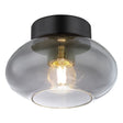 Moderne schwarze Deckenleuchte mit transparentem Rauchglasschirm und sichtbarer Glühfadenlampe, schräg von unten fotografiert.