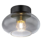Moderne schwarze Deckenleuchte mit transparentem Rauchglasschirm und sichtbarer Glühfadenlampe, schräg von unten fotografiert.