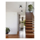 Globe Smoke Deckenleuchte in einem modernen Interieur mit Holztreppe und weißen Wänden, vom Flur in Richtung Küche gesehen.