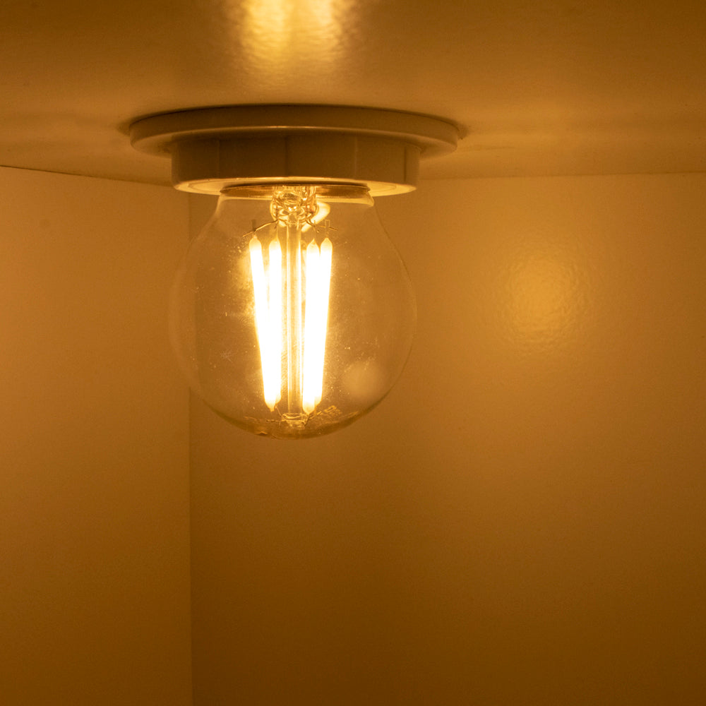Warmweiß brennende LED-Filamentlampe in Deckenleuchte, von unten betrachtet in einer Raumecke mit warmer Beleuchtung.