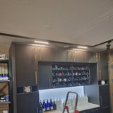 Moderner Wandschrank mit schwarzer Oberfläche und goldfarbenen Griffen, integrierter LED-Beleuchtung oben und offenen Regalen gefüllt mit Pflegeprodukten; Vorderansicht in einem professionellen Salon-Setting.
