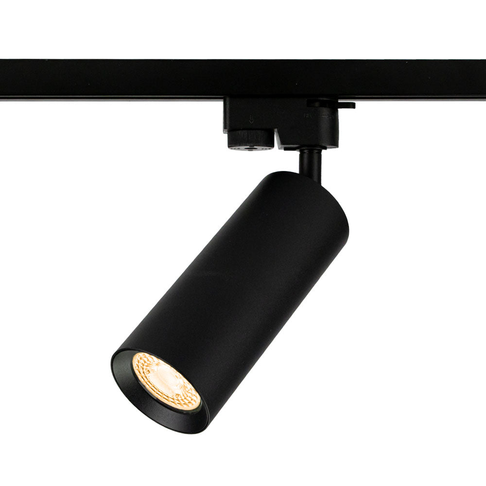 Schwarzer zylindrischer LED-Schienenstrahler mit warmweißem Licht, montiert auf einer schwarzen Spannschiene, schräg von vorne abgebildet.
