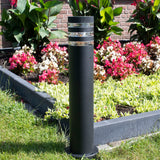 Eine moderne schwarze Gartenleuchte mit rundem Sockel, positioniert in einem farbenfrohen Blumengarten – Vorderansicht bei Tageslicht.