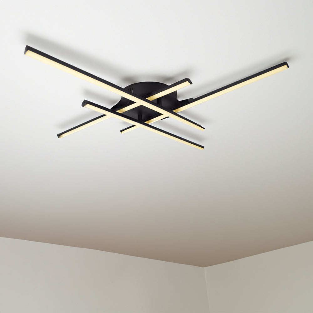Moderne schwarze Deckenleuchte mit kreuzförmigem LED-Design, montiert an einer weißen Decke, fotografiert aus einer Untersichtsperspektive.