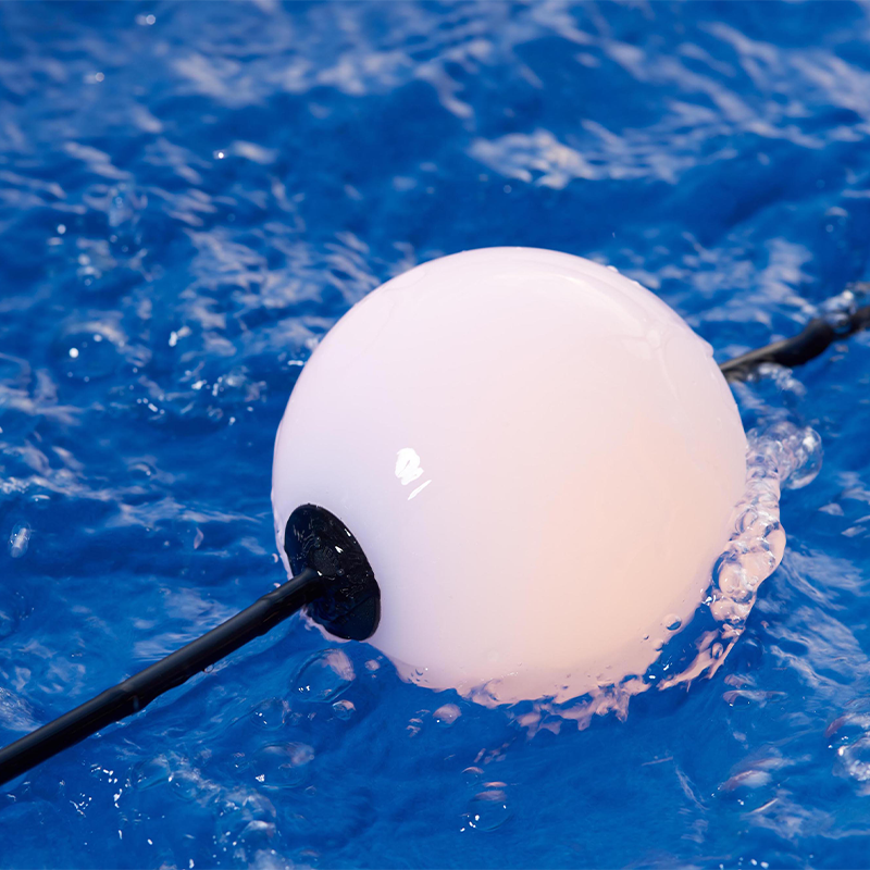 Weißes schwimmendes kugelförmiges LED-Poollicht, verbunden mit einem schwarzen Kabel, schwimmt auf plätscherndem blauem Wasser – Nahaufnahme von der Seite.