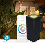 Frontansicht der smarten Außenleuchte Nedis SmartLife in Schwarz, abgebildet neben einem Smartphone mit zugehöriger App-Oberfläche zur Lichteinstellung, im Hintergrund ein moderner Garten und eine Hausfassade in der Dämmerung.