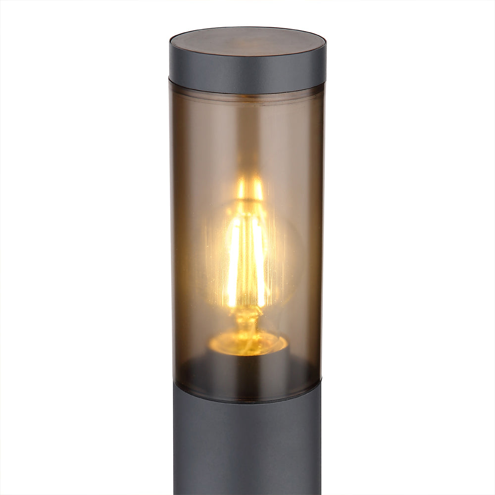 Nahaufnahme einer modernen Außenleuchte mit zylindrischem Design, schwarzem Gehäuse und warmem Bernsteinglas, in dem eine brennende LED-Glühbirne sichtbar ist.