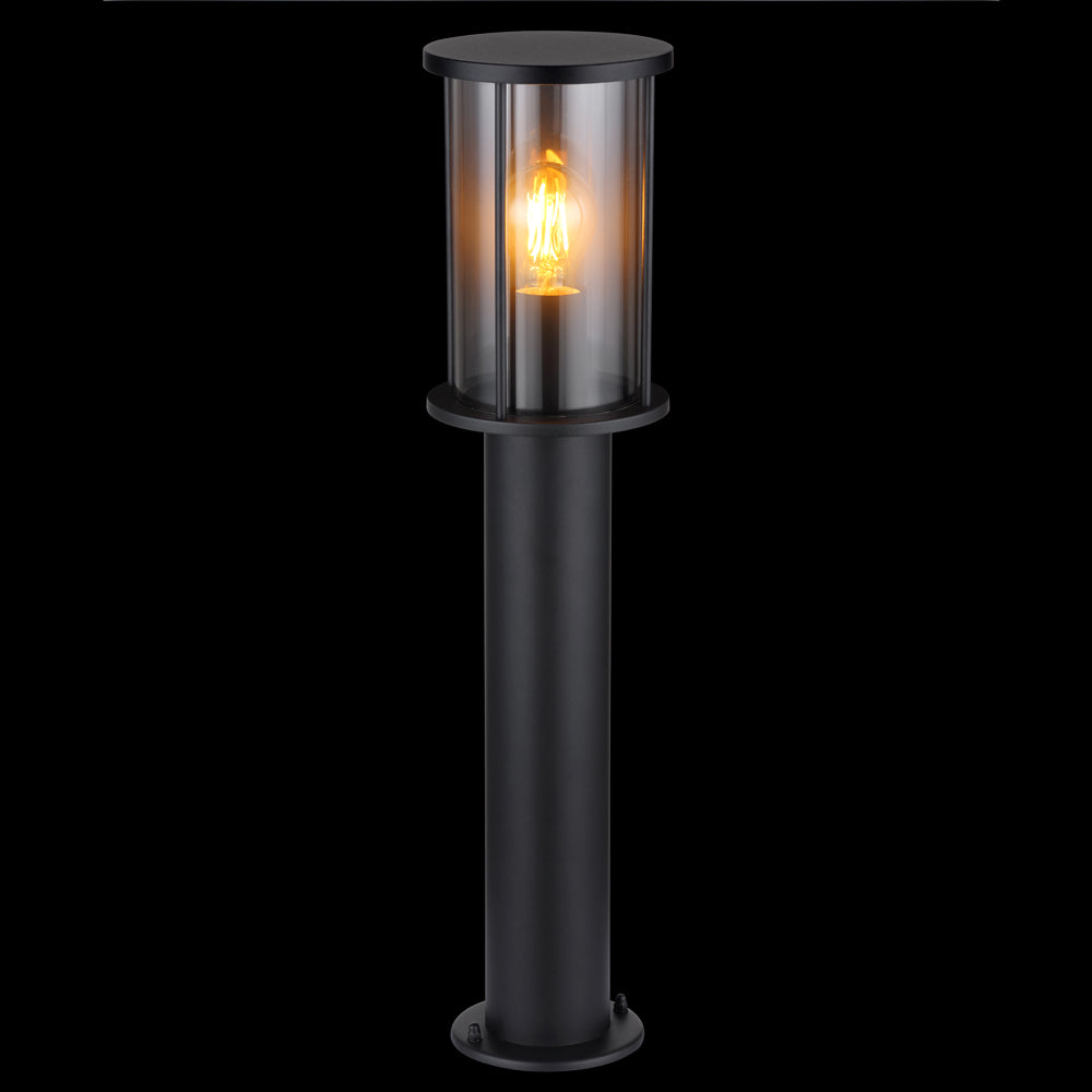 Stehende Außenleuchte im modernen schwarzen Design mit transparentem zylindrischem Schirm und sichtbarer Glühlampe, von vorne vor schwarzem Hintergrund fotografiert.