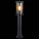 Stehende Außenleuchte im modernen schwarzen Design mit transparentem zylindrischem Schirm und sichtbarer Glühlampe, von vorne vor schwarzem Hintergrund fotografiert.