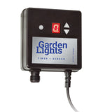 Vorderansicht des Garden Lights Timer + Sensor, ein schwarzes quadratisches Gerät mit digitaler Anzeige, Pfeiltasten und Anschlusspunkten für die Gartenbeleuchtung.