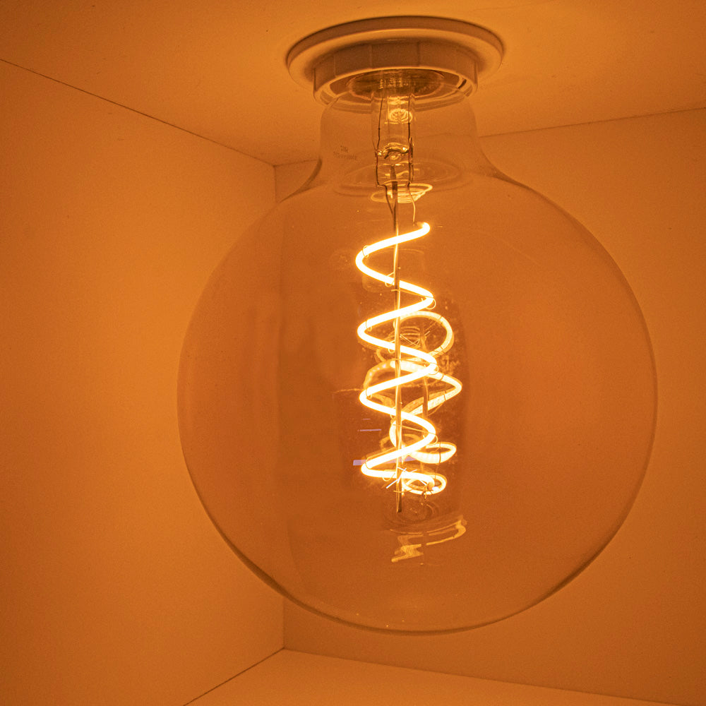 Große LED-Filamentlampe mit Spiralfaden, warmes Licht, von unten vor einer weißen Deckenhalterung fotografiert.