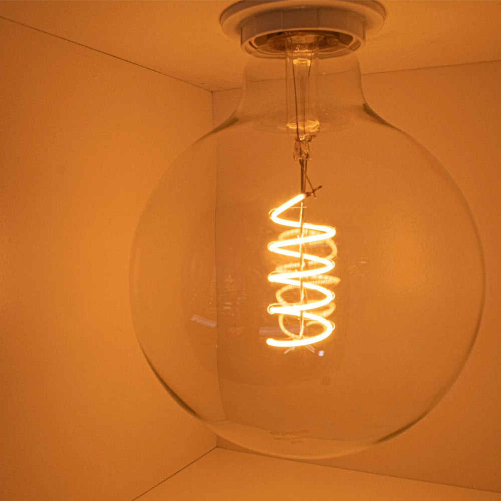 Nahaufnahme einer brennenden LED-Glühbirne mit Spiralfaden, an der Decke montiert, aus einer niedrigen Perspektive gesehen.