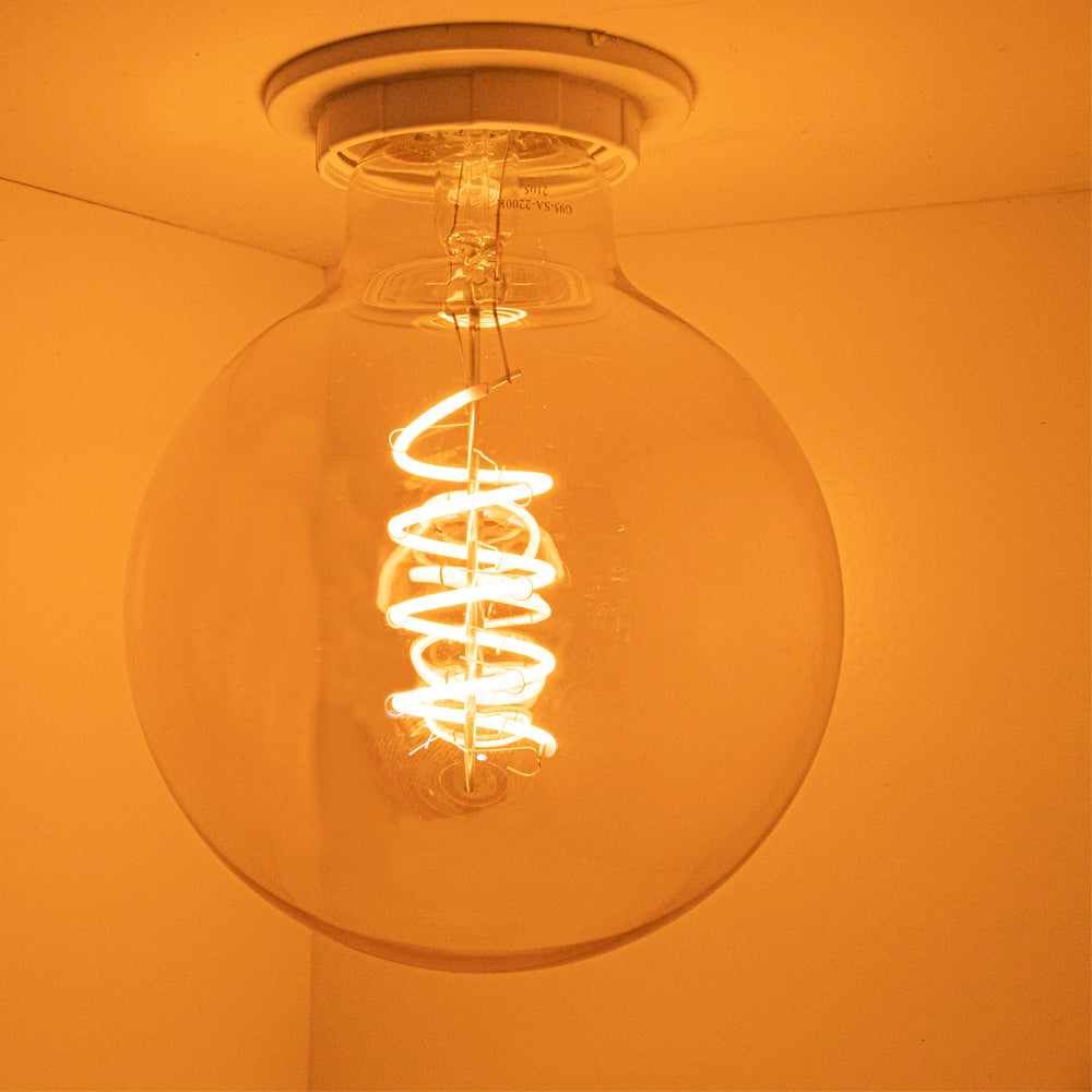 Nahaufnahme einer brennenden LED-Filament-Spirallampe an der Decke, von unten fotografiert mit warmweißem Licht und Retro-Design.
