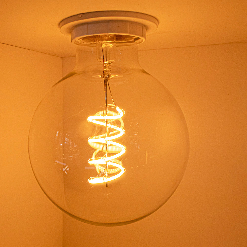 Nahaufnahme einer dekorativen Deckenleuchte mit einer runden E27-LED-Glühbirne aus Glas in einem warmen gelb-orangen Schein, von vorne gesehen.