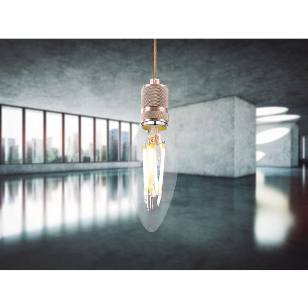 Nahaufnahme einer hängenden LED-Glühbirne in Kerzenform mit goldfarbener Fassung, ausgestellt in einem modernen Industrieraum mit großen Fenstern und Betonwänden; Vorderansicht der Lampe.