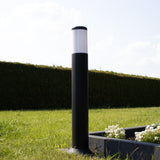Schwarze moderne Außenleuchte ARVA, Standmodell im Garten, Nahaufnahme von der Seite mit einem erhöhten Pflanzgefäß und einem gepflegten Rasen.