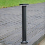 Eine moderne schwarze solarbetriebene Außenlampe in Standsockelform, fotografiert aus der perspektivischen Seitenansicht auf einer Holzterrasse mit Gras im Hintergrund.