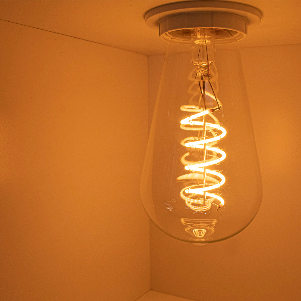 Nahaufnahme einer brennenden Retro-LED-Glühlampe mit Spiralfaden, an der Decke montiert und von schräg unten fotografiert.