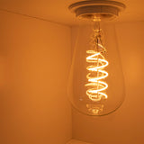 Nahaufnahme einer brennenden Retro-LED-Glühlampe mit Spiralfaden, an der Decke montiert und von schräg unten fotografiert.