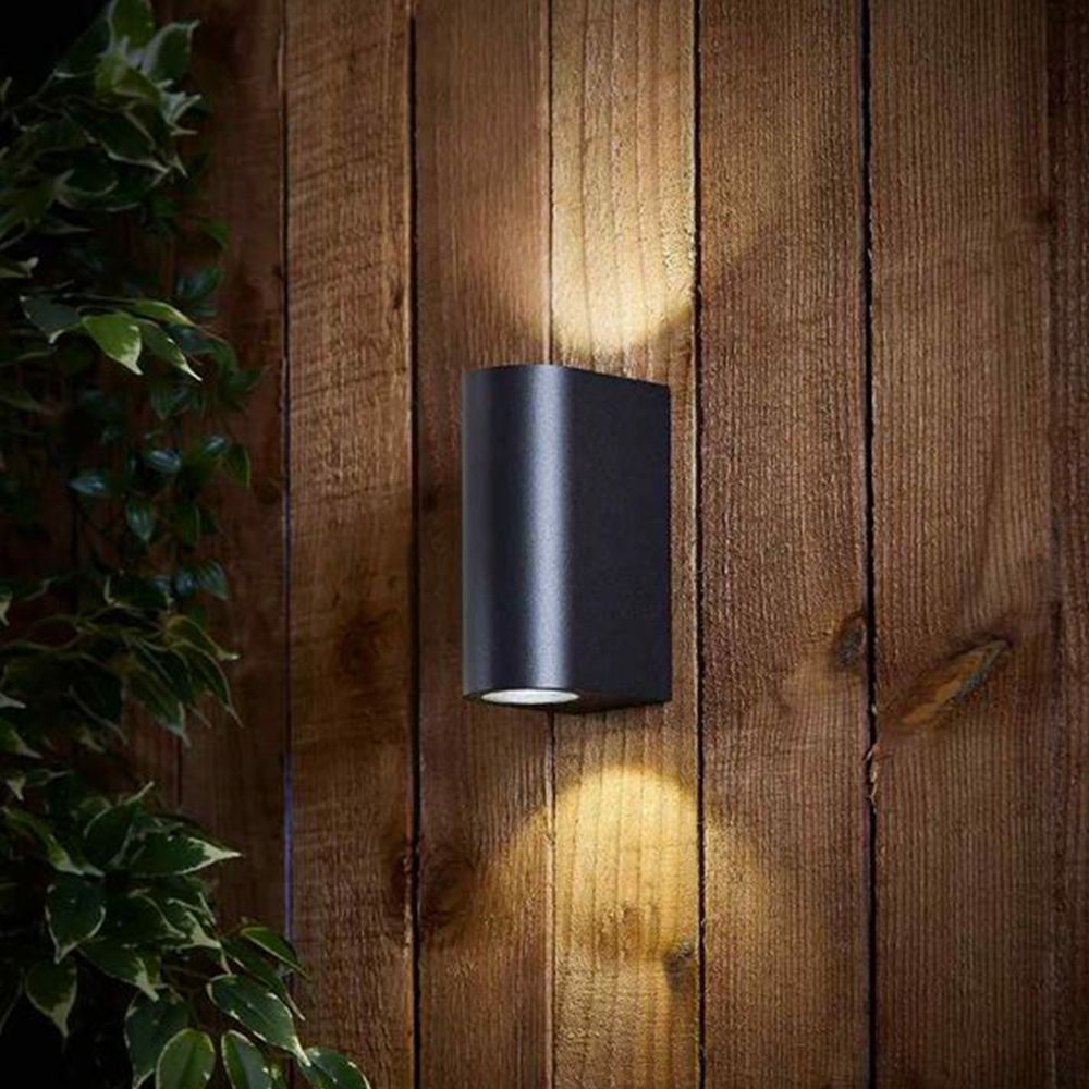 Schwarze moderne Up- und Downlight-Wandleuchte montiert an einer Holzaußenwand, Frontansicht, leuchtet sowohl nach oben als auch nach unten, geeignet zur Garten- oder Fassadenbeleuchtung.