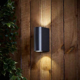 Schwarze moderne Up- und Downlight-Wandleuchte montiert an einer Holzaußenwand, Frontansicht, leuchtet sowohl nach oben als auch nach unten, geeignet zur Garten- oder Fassadenbeleuchtung.