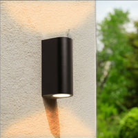 Schwarze, moderne LED-Außenwandleuchte mit warmer Auf- und Ab-Beleuchtung, montiert an einer hellen Außenwand, Seitenansicht.