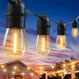 Nahaufnahme von wasserdichten LED-Partylichtern für den Außenbereich mit warmem Schein, die über einer Terrasse und einem Garten hängen und einen Blick auf ein Haus bei Sonnenuntergang bieten.