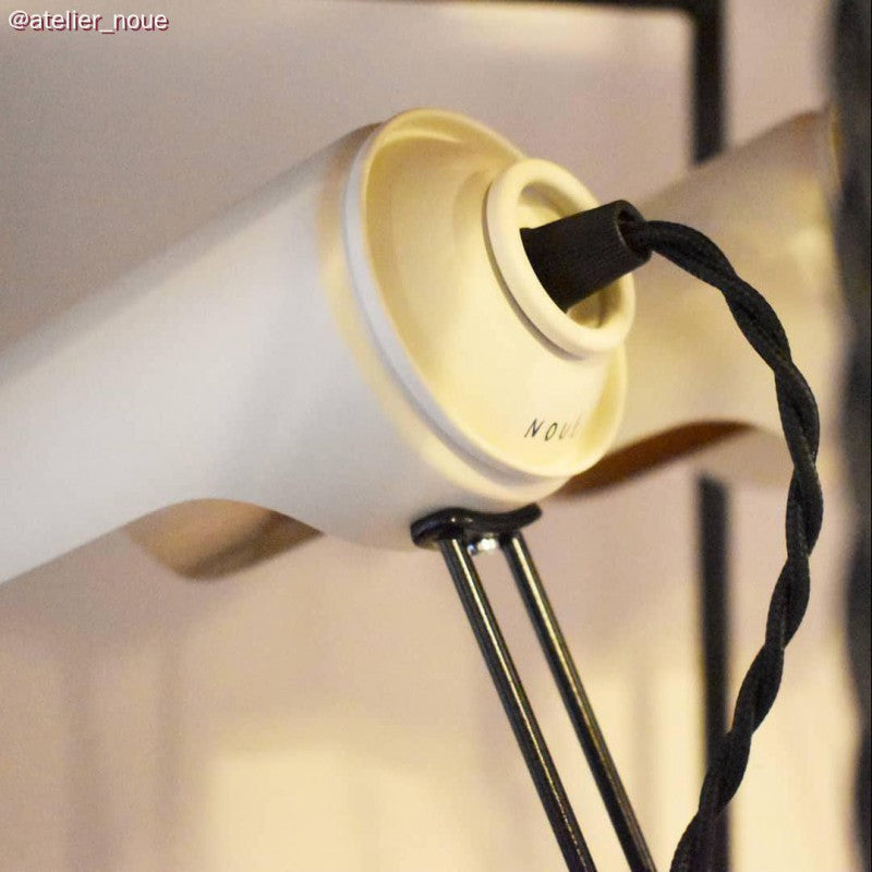 Nahaufnahme einer modernen weißen Wandlampe von Atelier Noue mit Keramikfassung, schwarzem Stoffkabel und Metallhalterung.