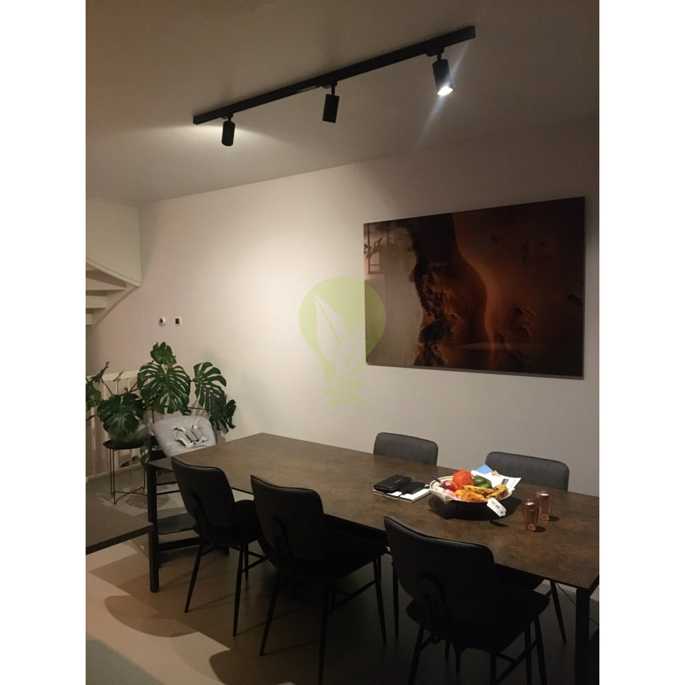 Schwarzer 3-Phasen-Schienenstrahler mit verstellbaren Spots, montiert an der Decke über einem Esstisch in einem modernen Esszimmer mit minimalistischem Interieur; Frontansicht der Schienenbeleuchtung im Einsatz.