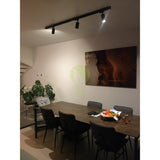 Schwarzer 3-Phasen-Schienenstrahler mit verstellbaren Spots, montiert an der Decke über einem Esstisch in einem modernen Esszimmer mit minimalistischem Interieur; Frontansicht der Schienenbeleuchtung im Einsatz.