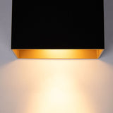 Nahaufnahme einer modernen schwarzen Wandlampe mit goldener Innenseite von unten, die warmweißes Licht nach unten abgibt.