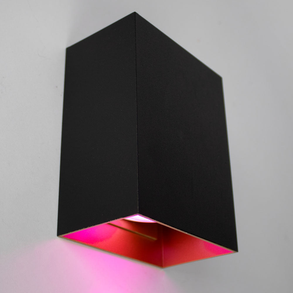 Mattschwarze, moderne Wandleuchte mit rechteckigem Design und rosa Beleuchtung unten, Seitenansicht auf einer weißen Wand.