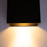 Schwarze Wandleuchte mit integrierter LED-Beleuchtung, von unten betrachtet, wobei warmweißes Licht nach unten gegen eine helle Wand strahlt.