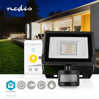 Vorderansicht des Nedis SmartLife LED-Flutlichts mit Bewegungssensor, abgebildet vor einem modernen Haus bei Nacht, mit der zugehörigen Smartphone-App-Schnittstelle zur Steuerung der intelligenten Beleuchtung.