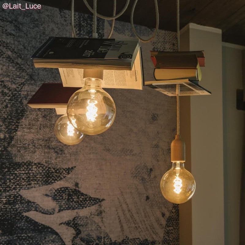 Eine Pendelleuchte mit Glühbirnen im Vintage-Look und Büchern als Deckenelemente, schräg von der Seite betrachtet vor einem stimmungsvollen Wandhintergrund – kreative und dekorative Beleuchtung für eine Bibliothek oder Leseecke.
